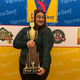 Winner of hot dog contest posing with giant hot dog trophy